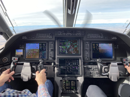 View of the Pilatus PC-12 NGX cockpit from behind, showcasing dual digital displays, flight controls, and modern avionics suite