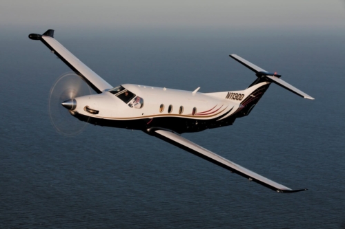 Pilatus PC-12 NGX turboprop aircraft flying low over sunlit desert dunes